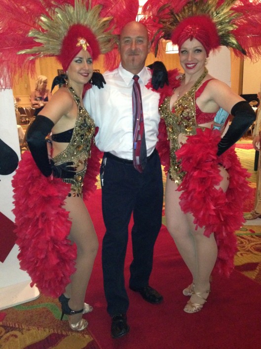 Vegas showgirls in gold and red, entertainer in middle